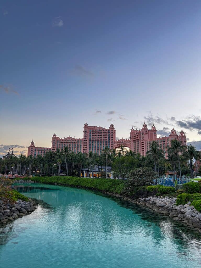 Atlantis Paradise Island resort at dusk reflected in turquoise lagoon waters, framed by palm trees in Nassau, Bahamas
