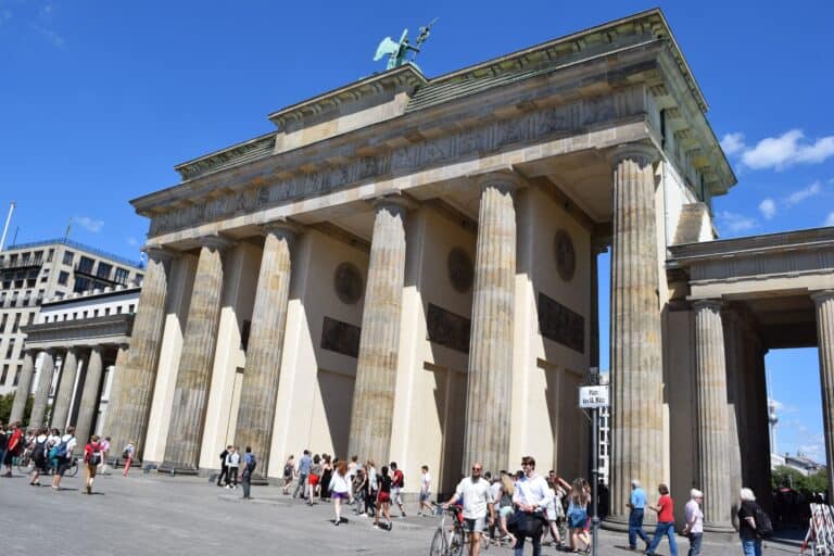 Looking up at the Brandenburg Gate columns from street level in Berlin, with the Victoria quadriga statue above and the Berlin TV tower visible to the right