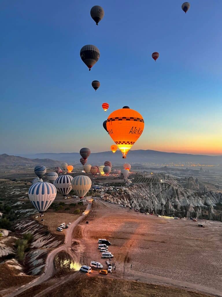 Glowing orange hot air balloon rising at dawn over Cappadocia's fairy chimney formations, Turkey