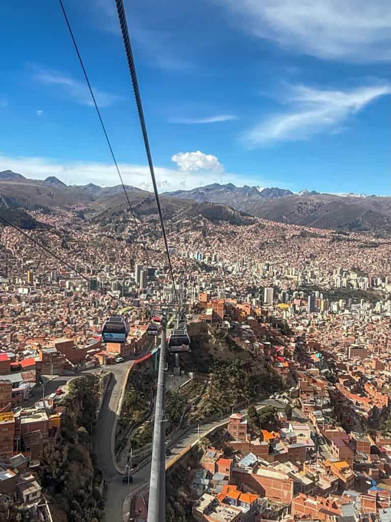Looking down from the Mi Teleférico cable car over the densely packed terracotta rooftops of La Paz filling a mountain valley, with the Andes peaks visible on the horizon, Bolivia