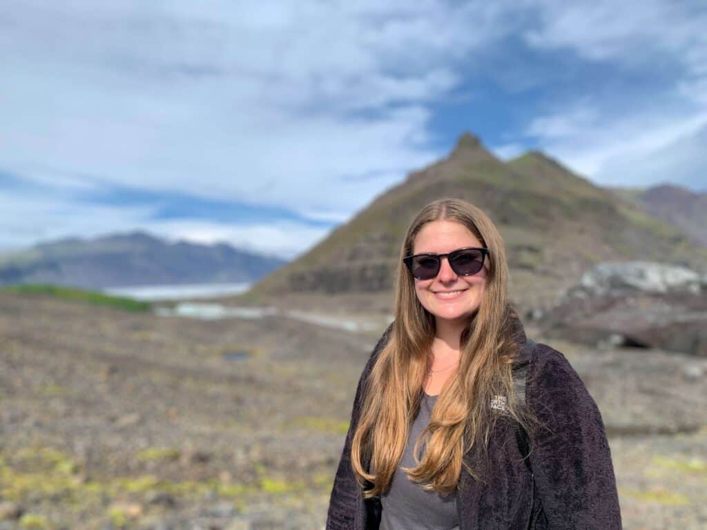 Kaitlin smiling in front of a volcanic Icelandic landscape with rugged mountains and glacier behind