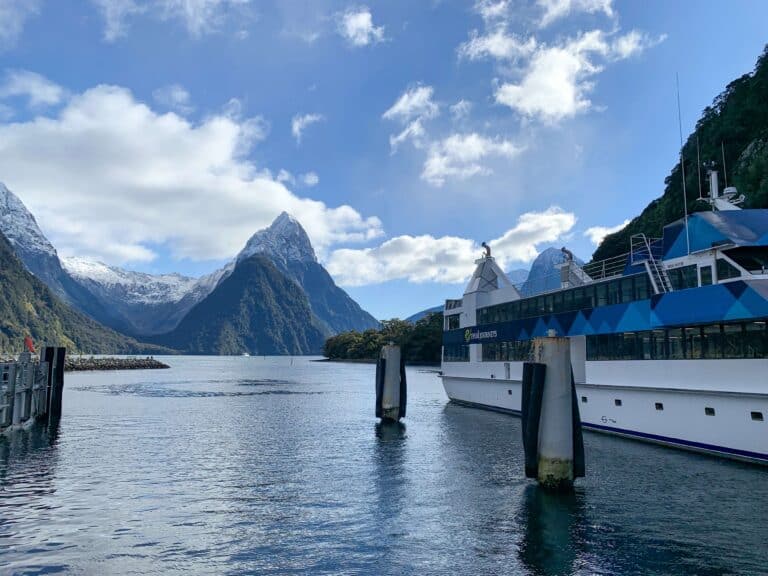Mitre Peak rising above Milford Sound fiord with a Real Journeys cruise vessel docked in the foreground and snow-capped mountains behind, Fiordland, New Zealand