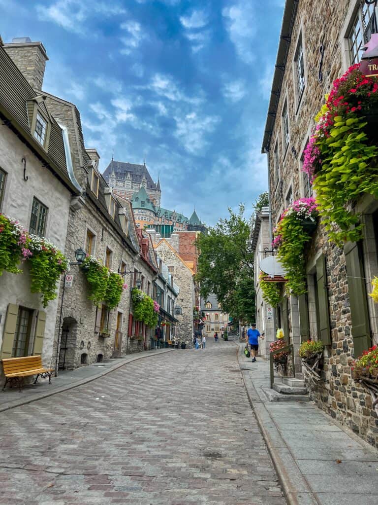 Cobblestone street in Old Quebec City with Château Frontenac rising above stone buildings with summer flower boxes