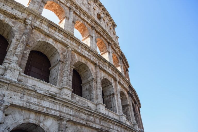 Low-angle close-up of the Colosseum exterior arches and columns in Rome, Italy, against a clear blue sky