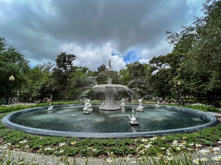Forsyth Park fountain in Savannah, Georgia surrounded by live oak trees under dramatic storm clouds, with white daisies in the foreground