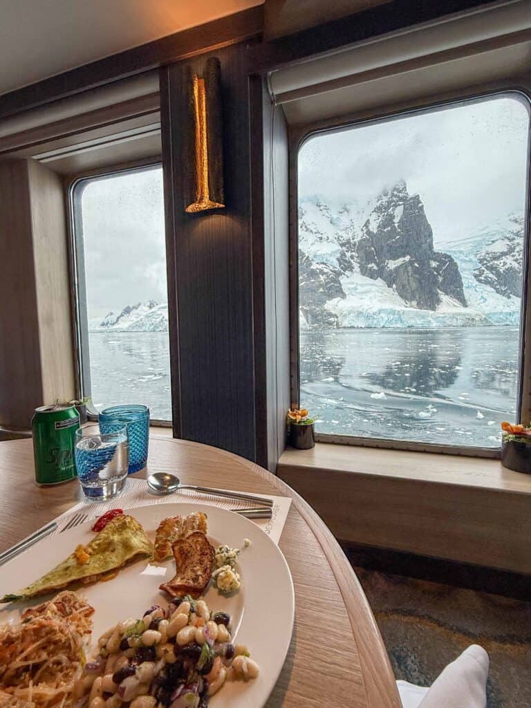 Dining table with a plated meal, Antarctic mountains and glacier visible through the window