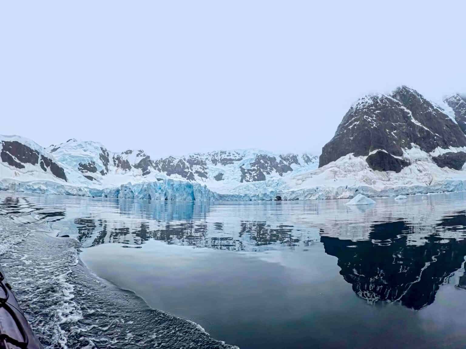 What to expect in Antarctica: zodiac view of calm water and Peninsula mountains reflected.