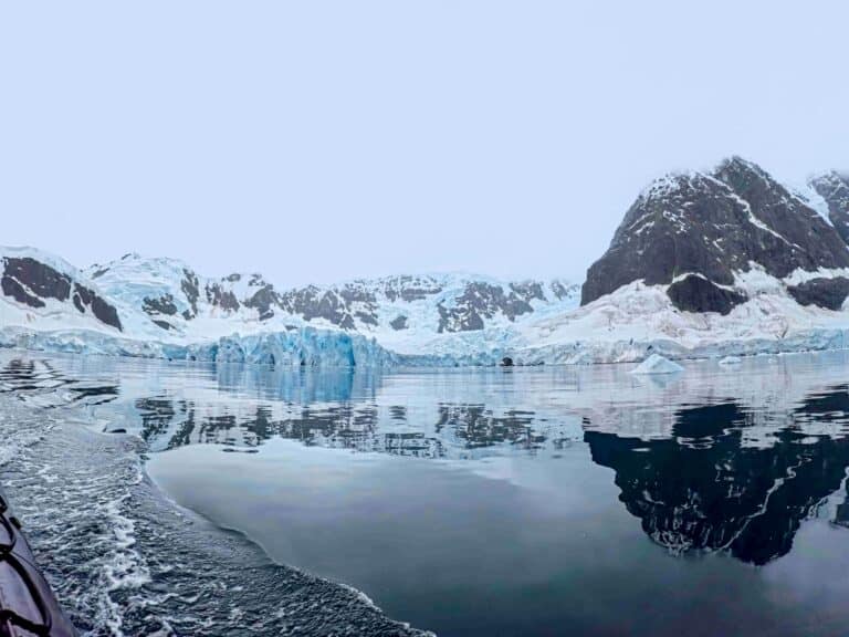 What to expect in Antarctica: zodiac view of calm water and Peninsula mountains reflected.