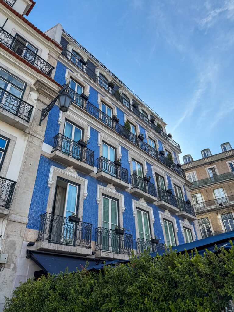 Blue and white azulejo-tiled apartment building facade in Lisbon, viewed from street level looking up.