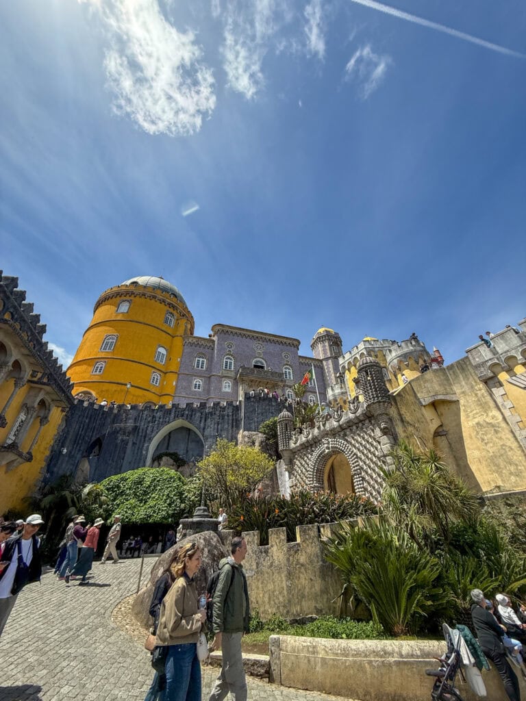 Pena Palace exterior in Sintra, Portugal, showing the yellow tower and gray tiled facade against a clear sky.
